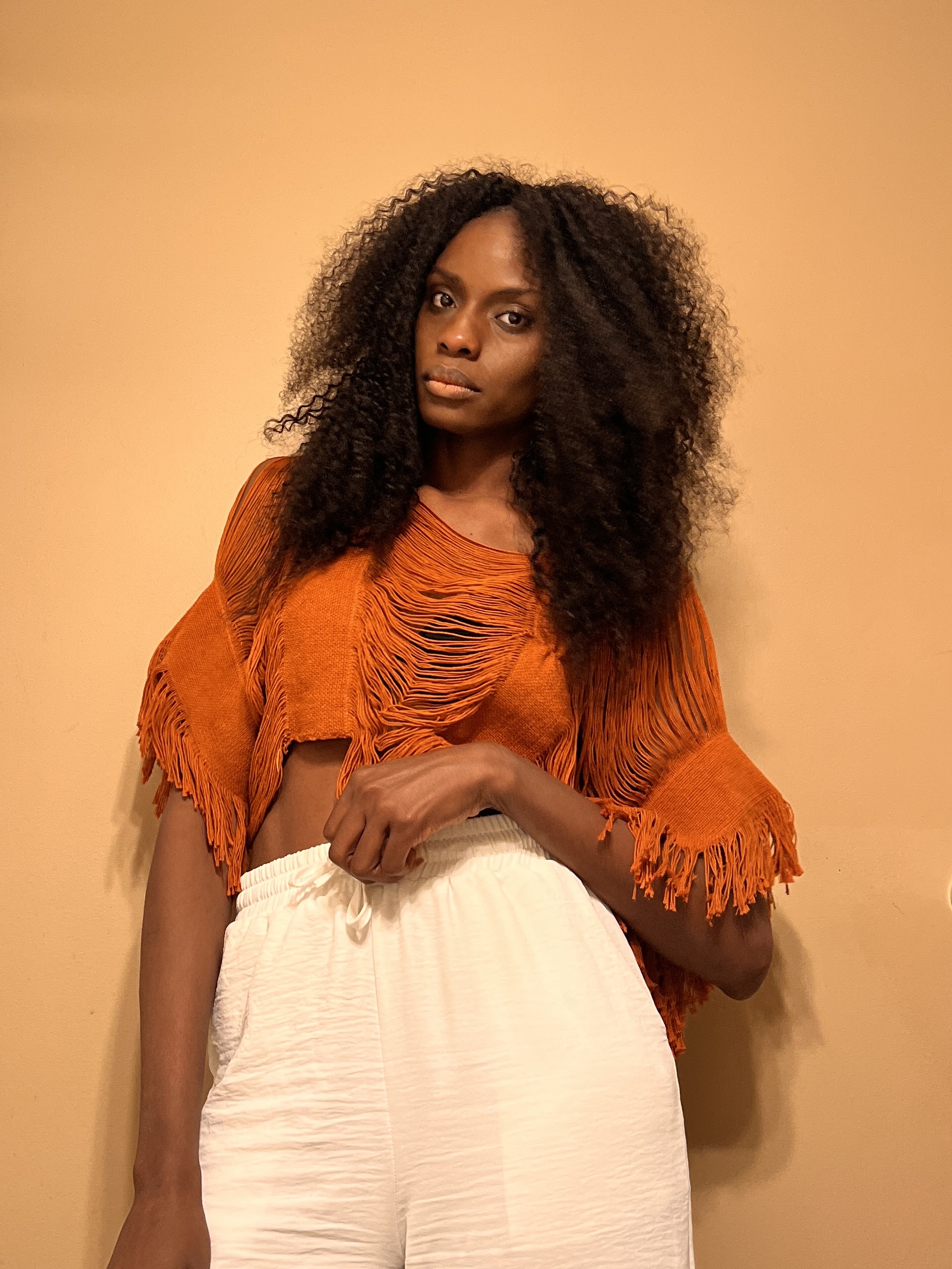 Jeronique poses with long thick hairstyle in orange top and white pants